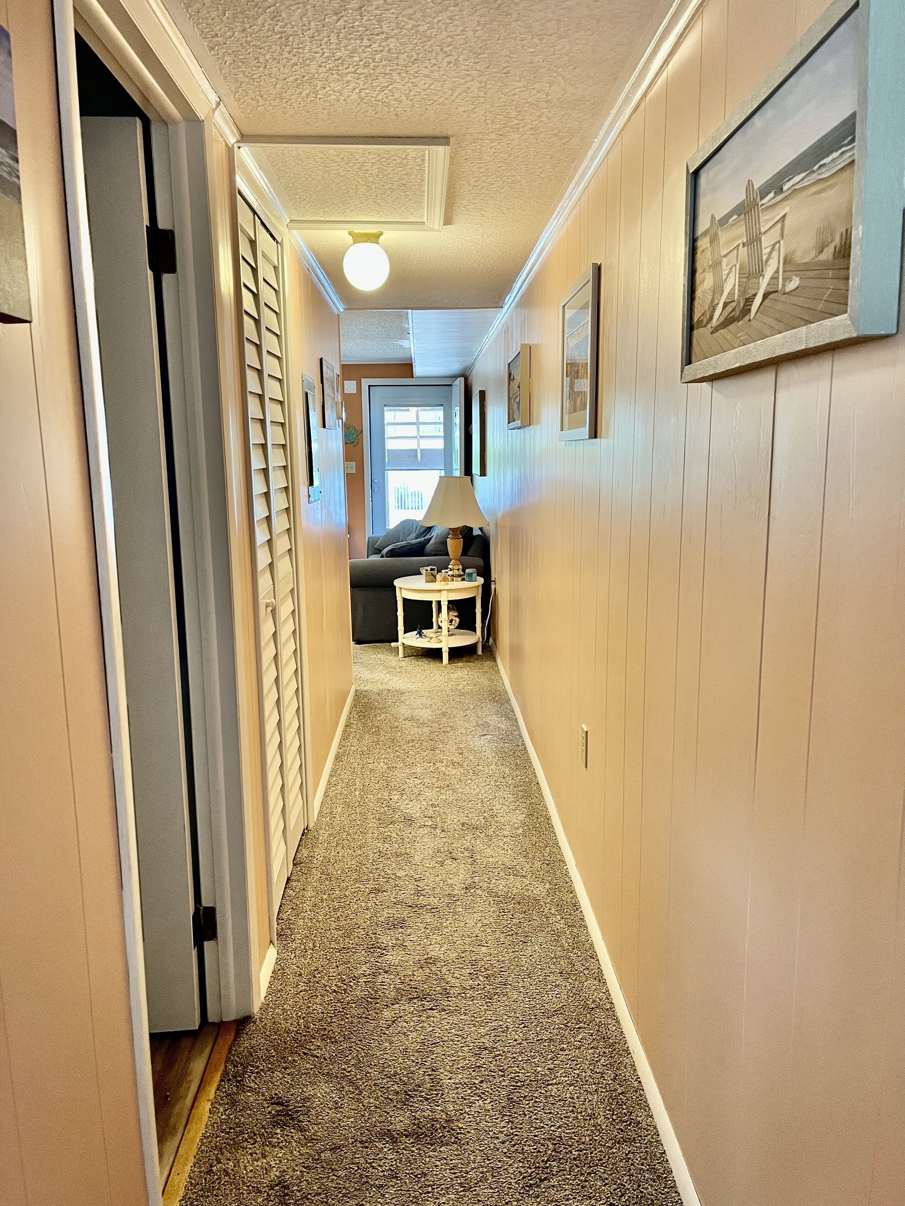 A narrow hallway with a carpeted floor, a small round table with a lamp, and a door on the left.