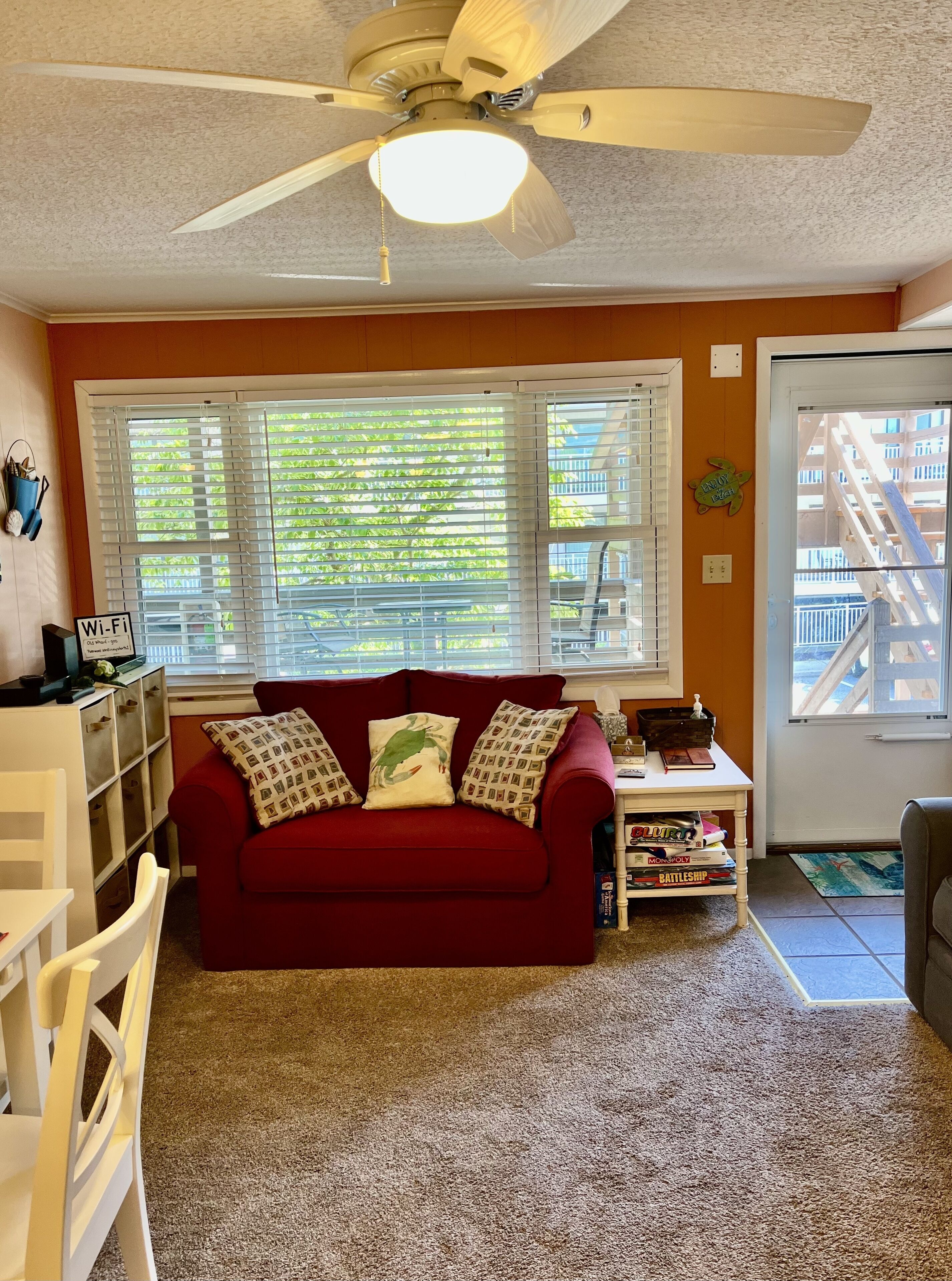 A living room with a red couch, a ceiling fan, and a window with blinds.