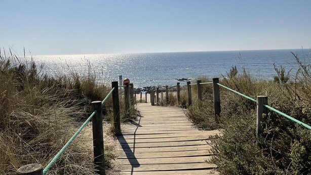 Eine hölzerne Promenade führt zum Strand mit freiem Blick auf den Ozean.
