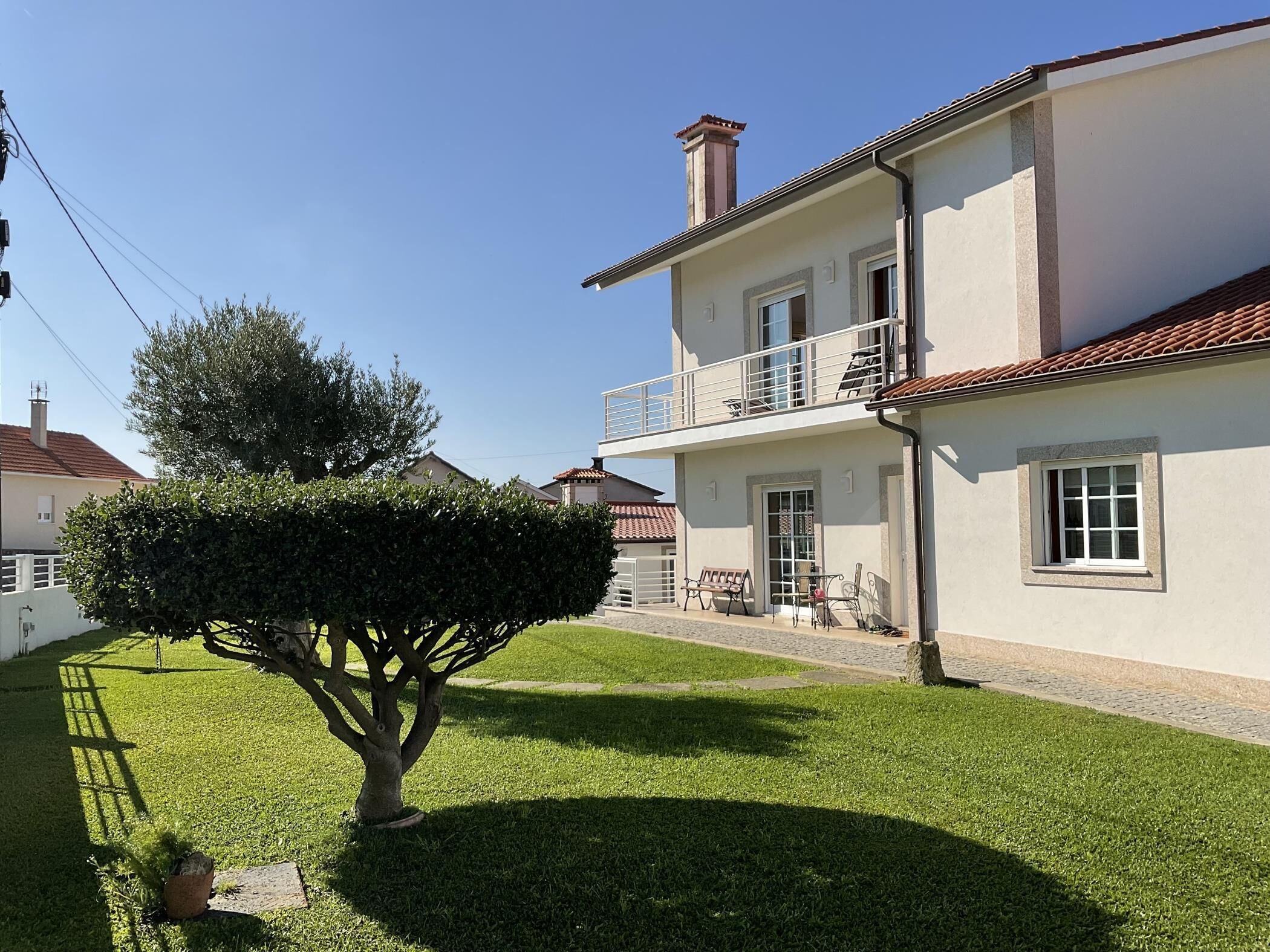 A two-story house with a balcony, a well-maintained lawn, and a tree.