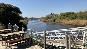 Eine Holzterrasse am Flussufer mit Picknicktischen und einem Seilgeländer.