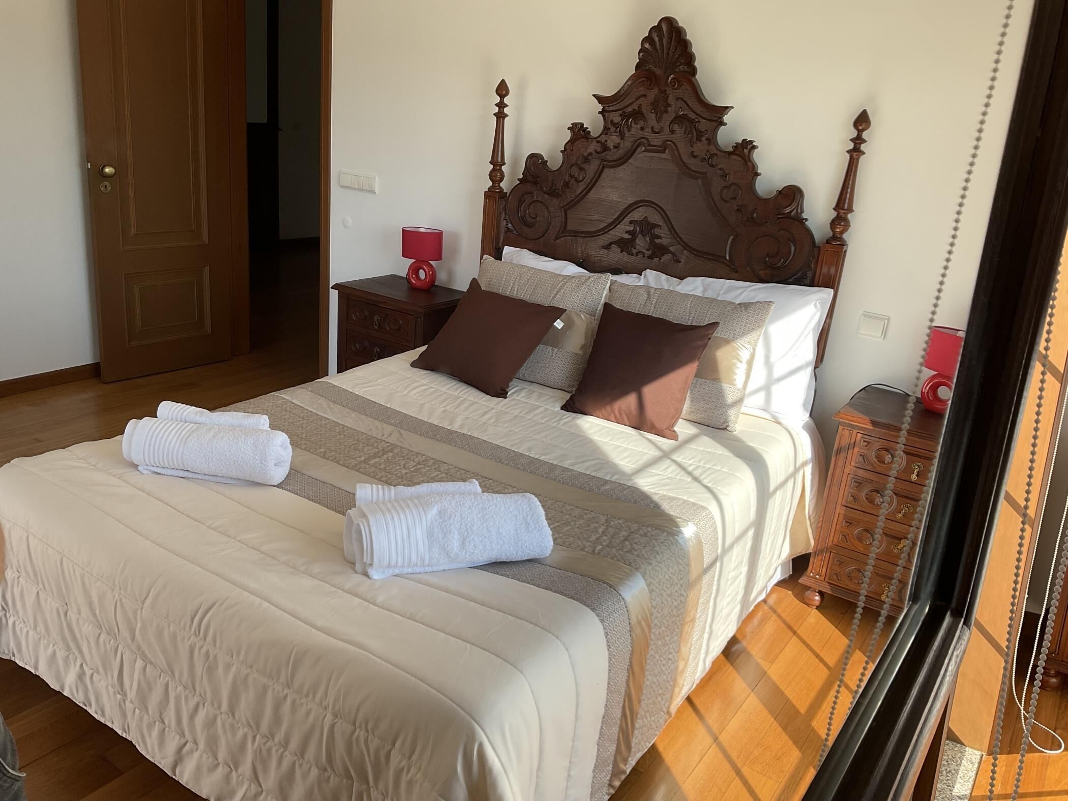 A neatly made bed with a wooden headboard, a bedside table with a lamp, and a wooden nightstand.