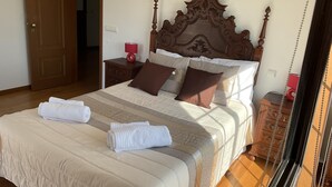 Ein ordentlich bezogenes Bett mit einem Holz-Kopfteil, ein Nachttisch mit Lampe und ein weiterer Nachttisch aus Holz.