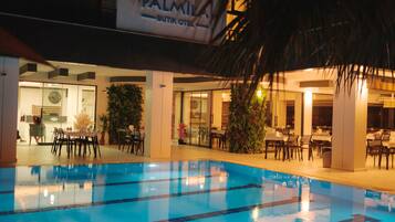 Una piscina interior con agua cristalina, rodeada de mesas y sillas, y un cartel que dice "PALMIYA BUTIK OTEK".