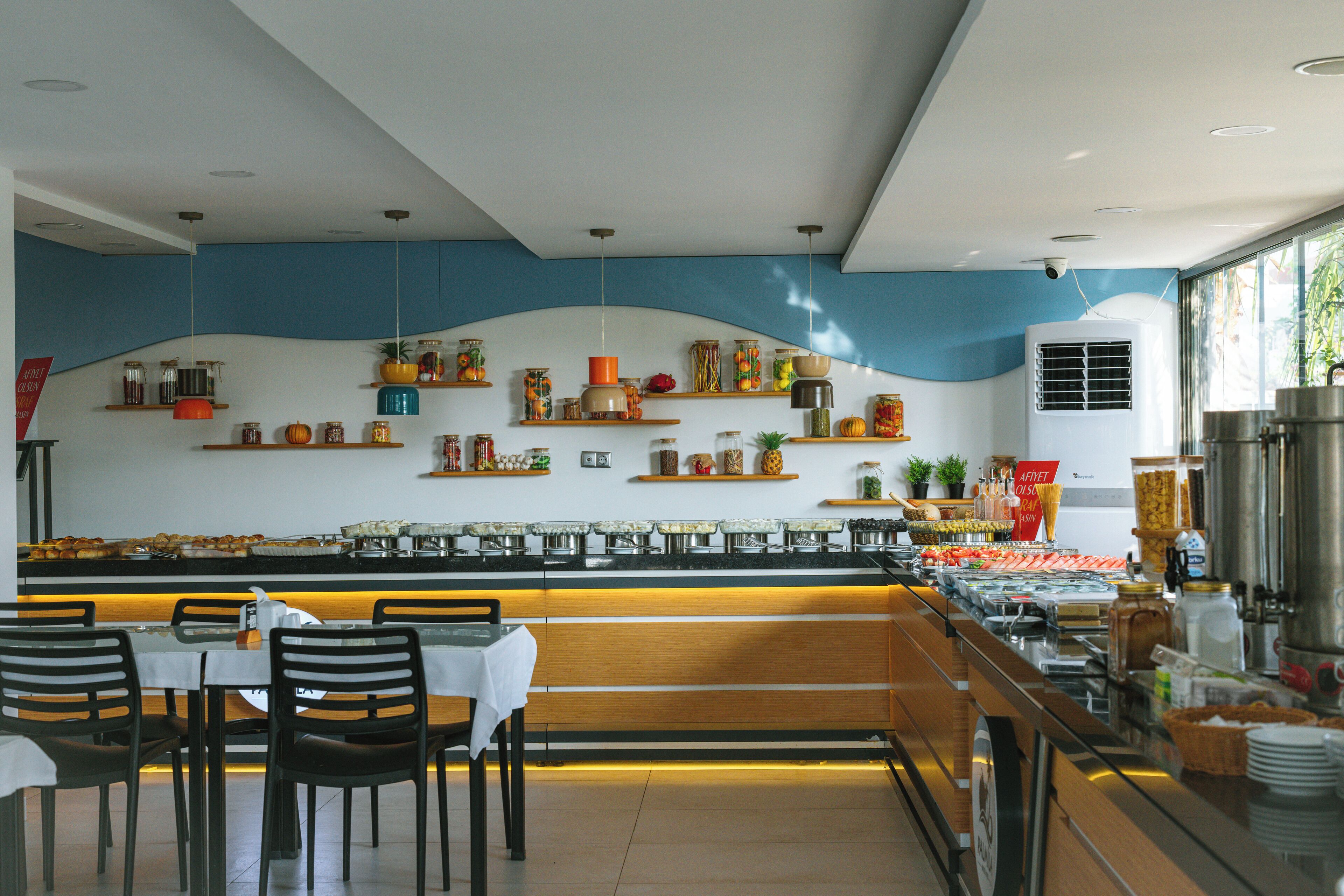 A buffet area with a variety of food items, a counter with a glass barrier, and seating with tables and chairs.