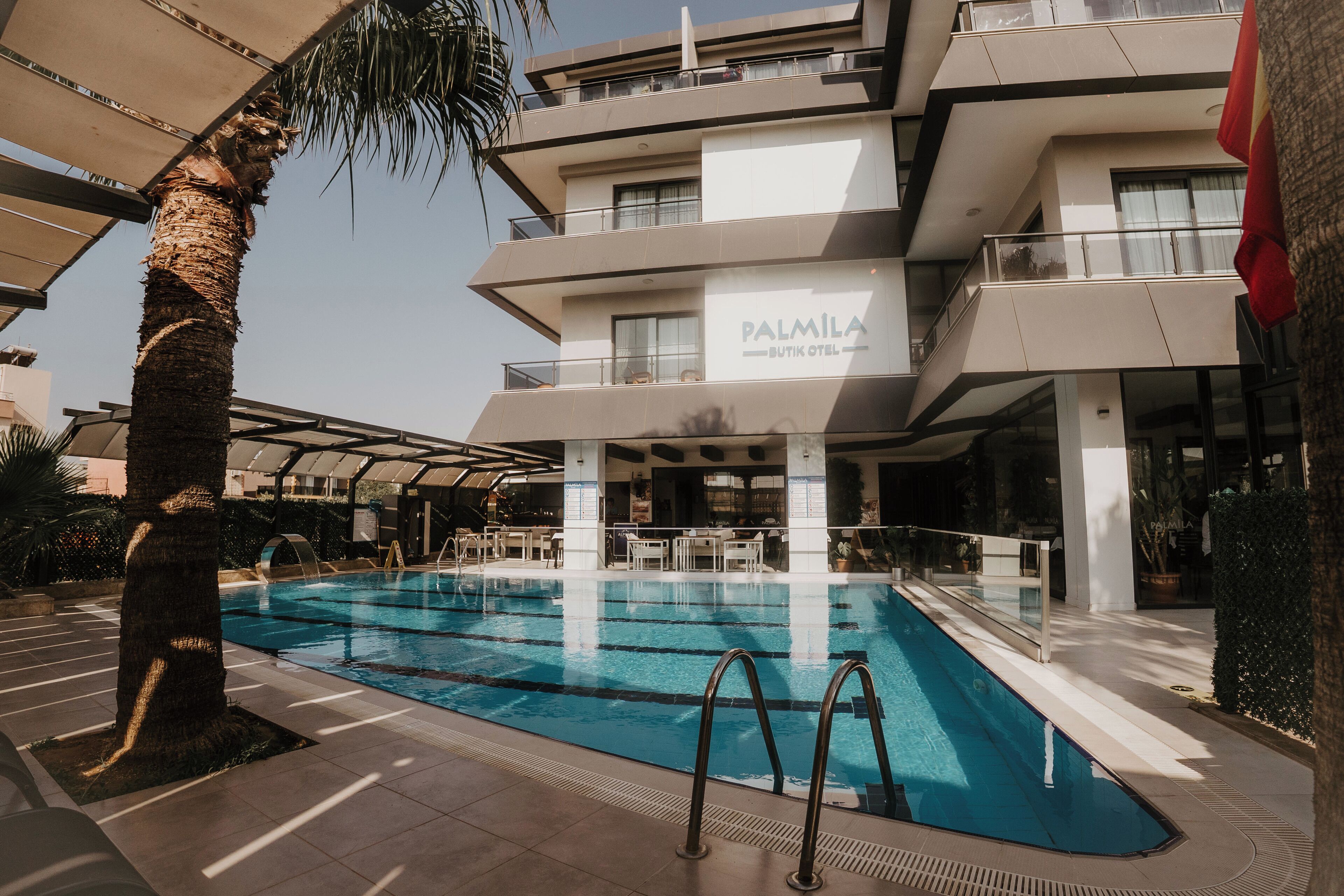 Un hotel moderno con zona de piscina, asientos al aire libre y una palmera.