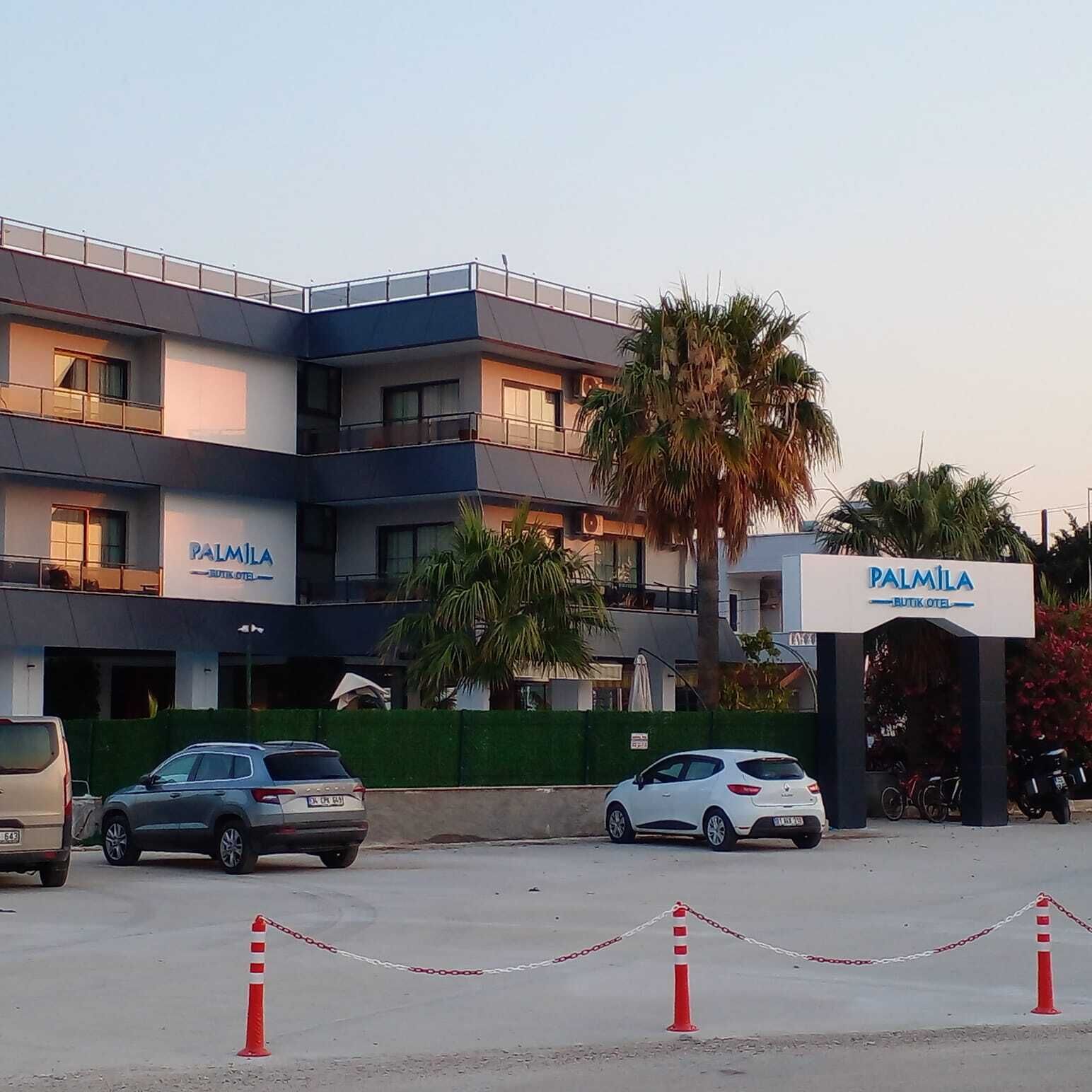 A multi-story hotel named 'PALMILA' with a modern design, featuring balconies and a gated entrance.