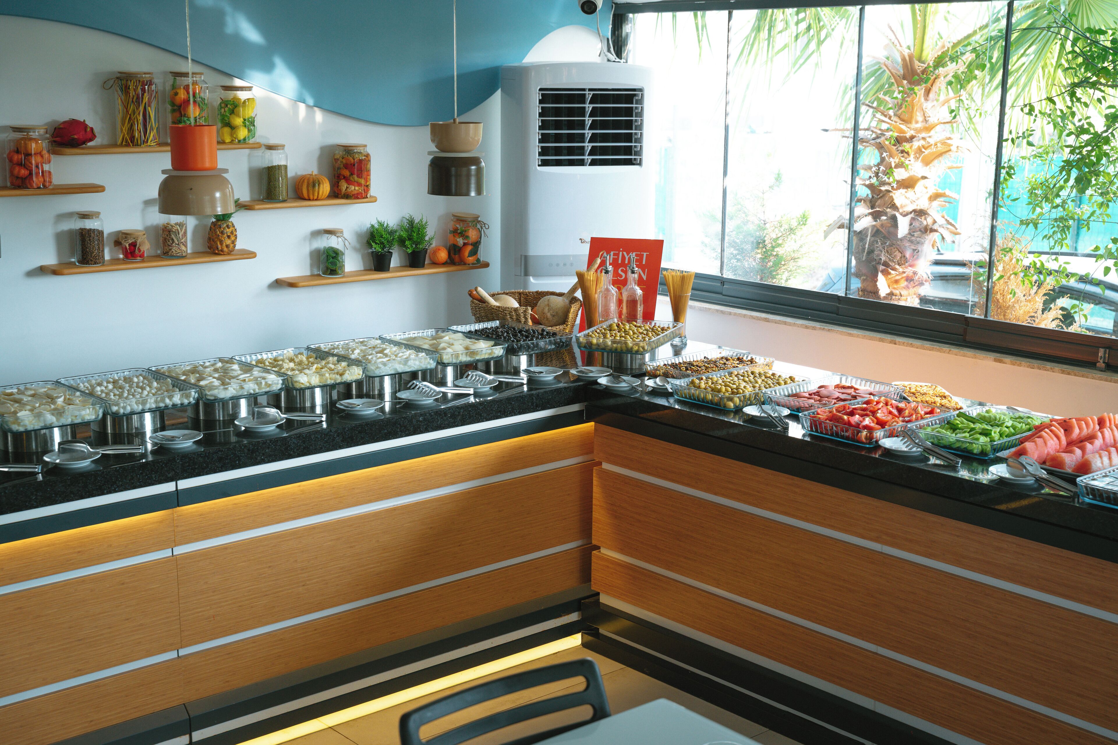 A buffet area with various food items and a window with a view of palm trees.