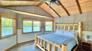 A wooden-framed bedroom with a bed, windows, and a ceiling fan.
