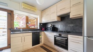 A modern kitchen with light wood cabinets, a black countertop, stainless steel appliances, and a window with a view of the outside. - 10 minutes from Budapest Family apartment (Törökbálint)