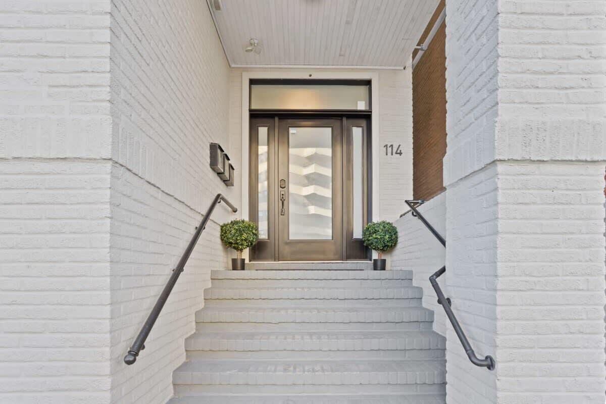 Un bâtiment en briques blanches, avec un escalier menant à une porte portant le numéro 114.