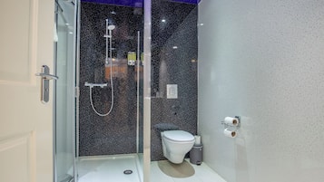 A modern bathroom with a glass-enclosed shower, a toilet, and a wall-mounted toilet paper holder.