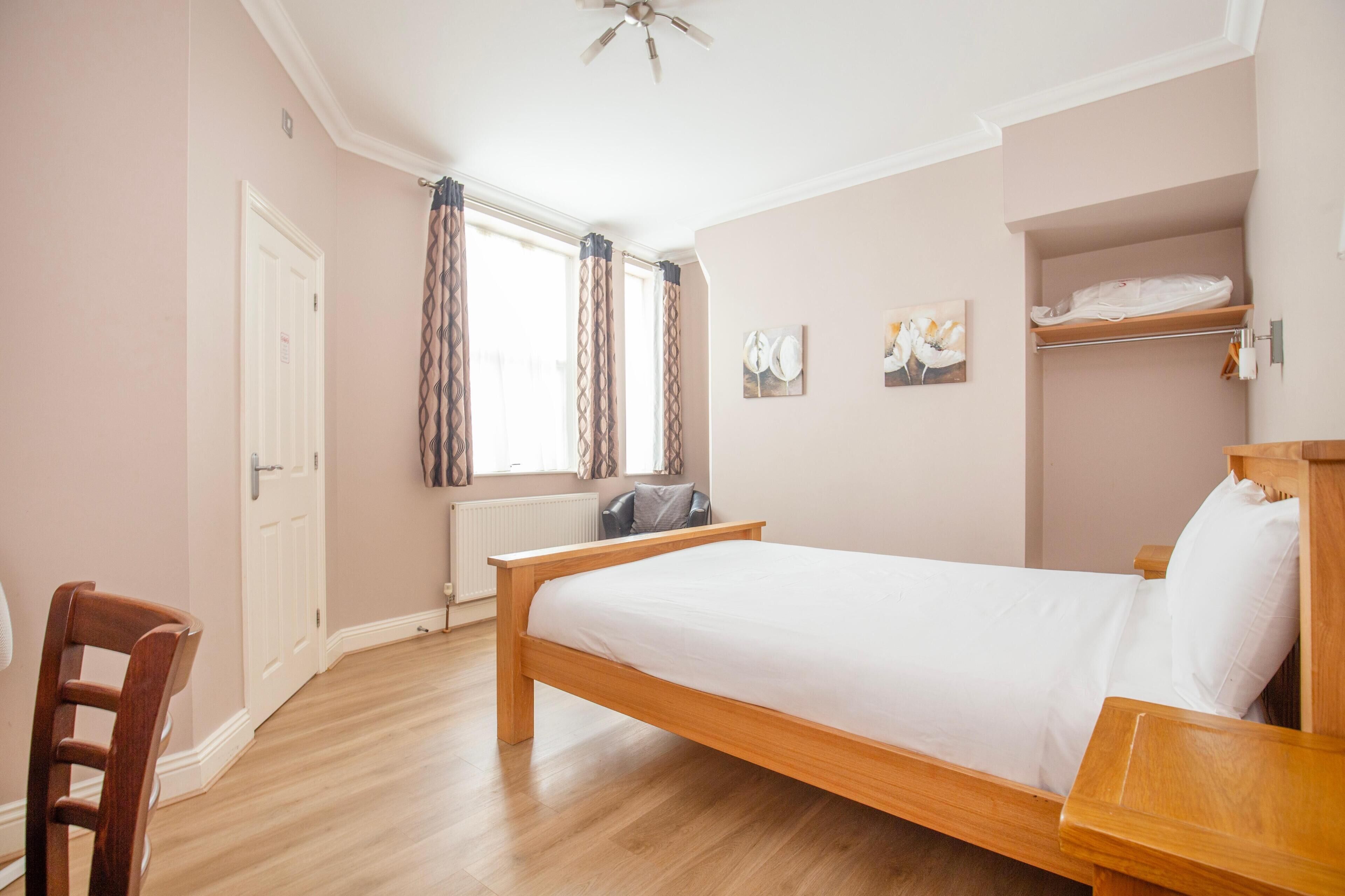 A bedroom with a wooden bed, a chair, a radiator, a window with curtains, and a ceiling fan.