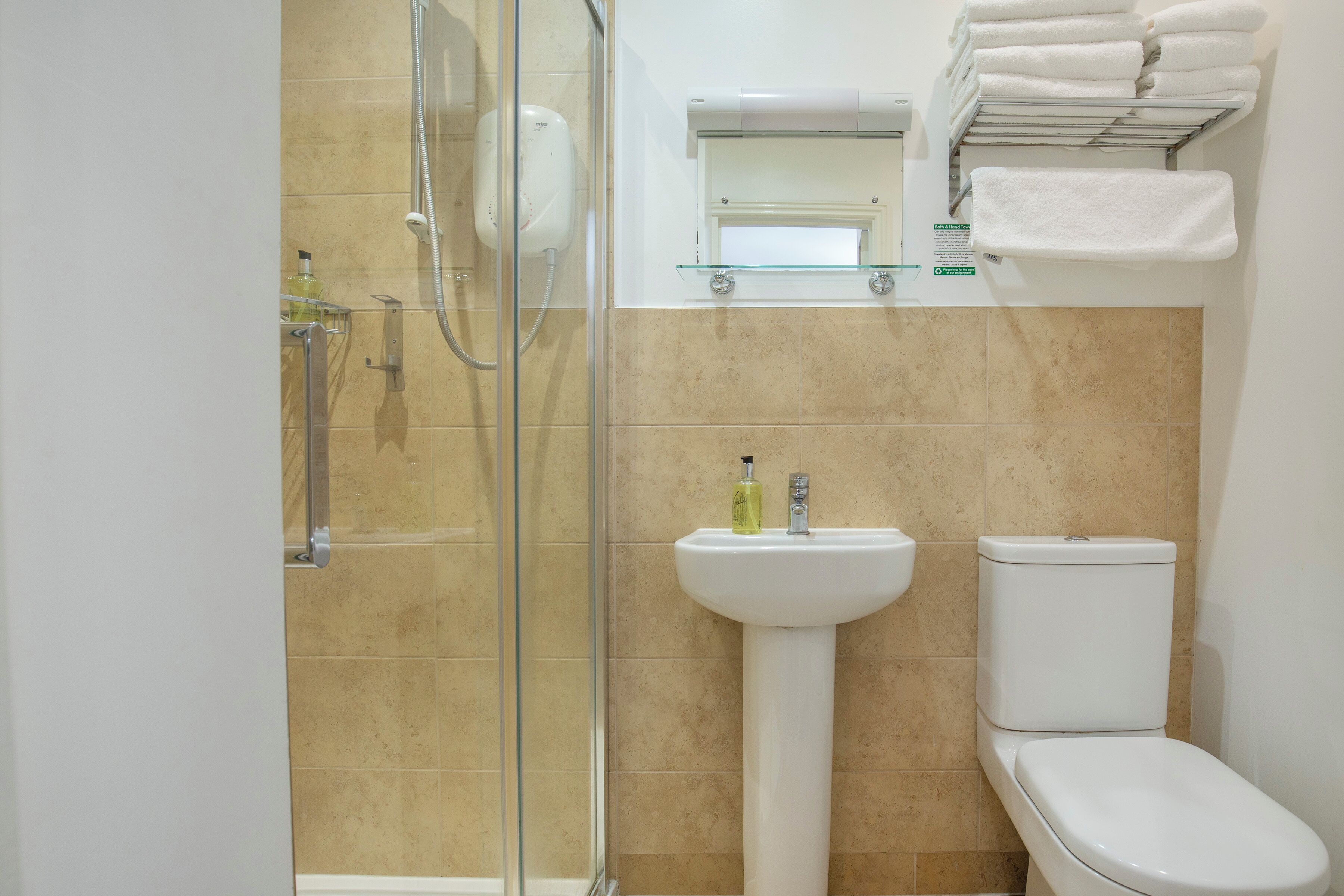 A bathroom with a glass shower enclosure, a pedestal sink, a toilet, and a glass shelf with folded towels.