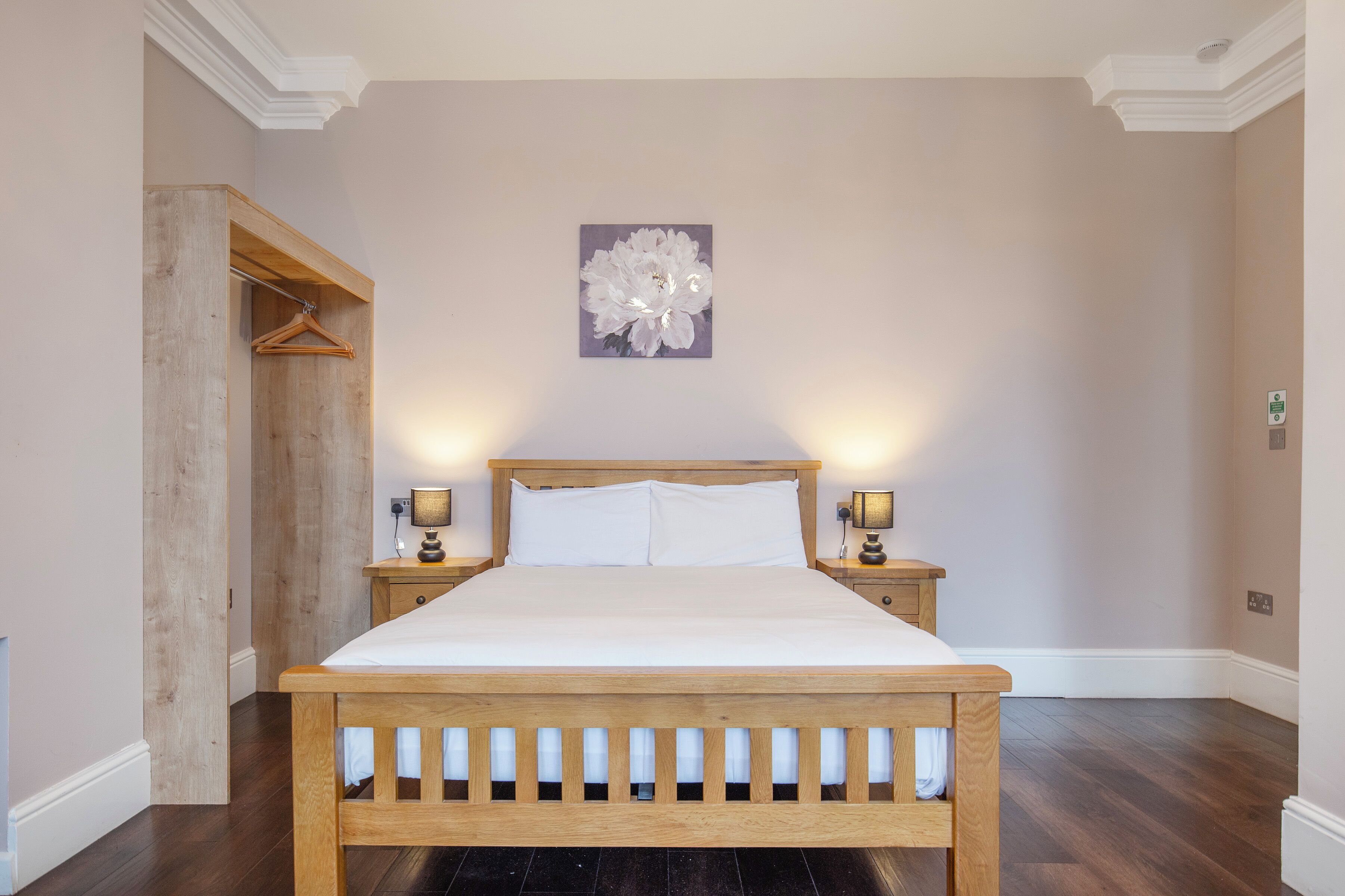 A bedroom with a wooden bed, two bedside tables with lamps, a wall-mounted artwork, and a wooden wardrobe.