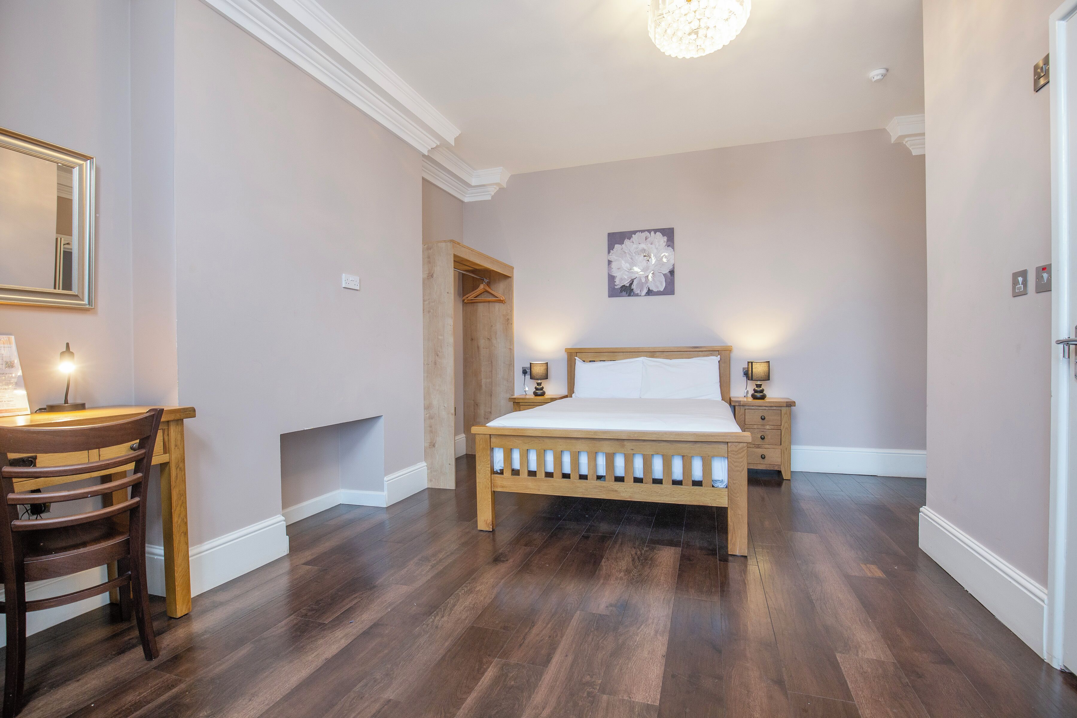 A bedroom with a wooden bed, bedside lamps, a wooden chair, a mirror, and a door.