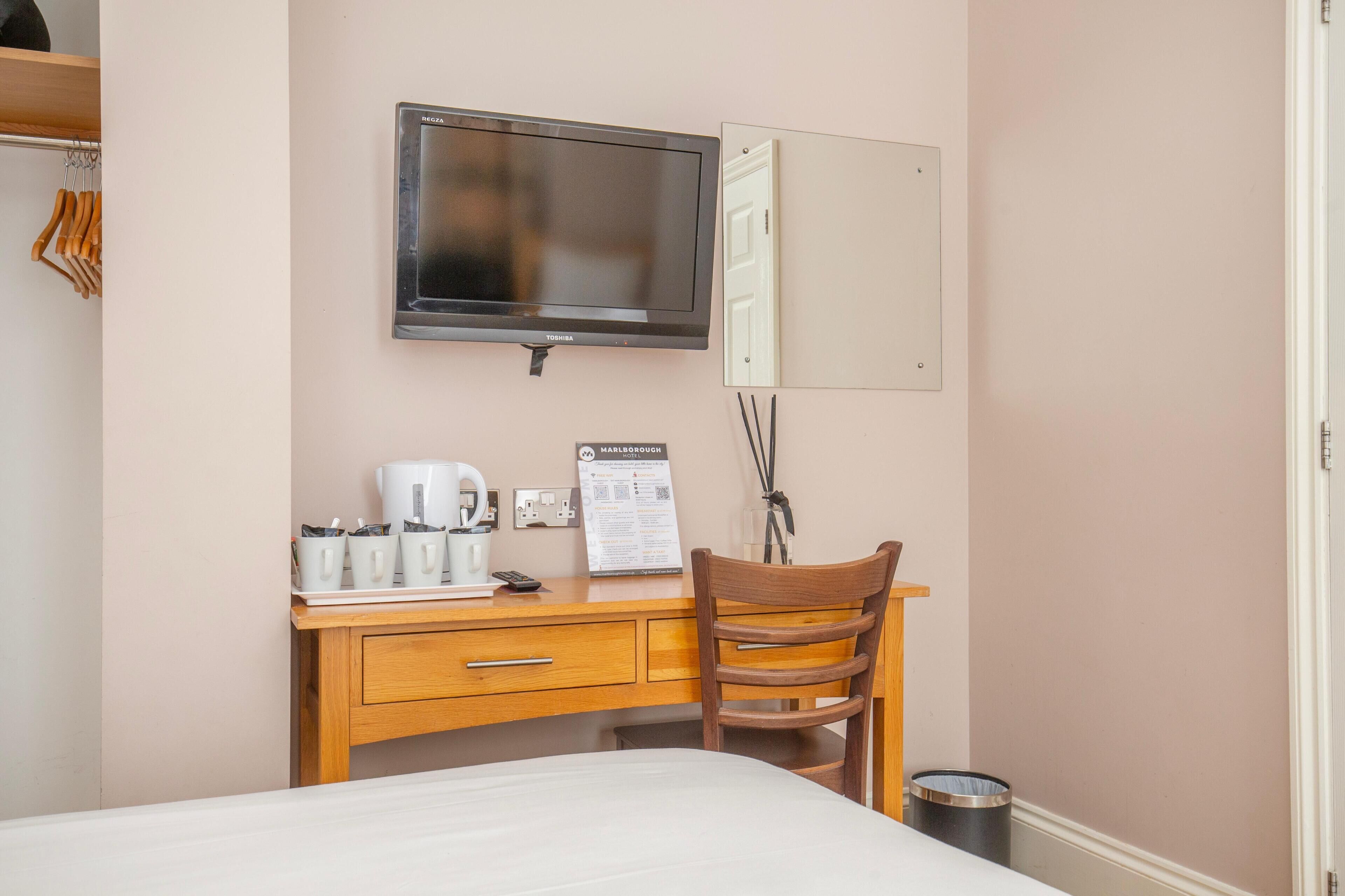 A hotel room with a bed, a desk with a chair, a television, a coffee maker, and a trash can.