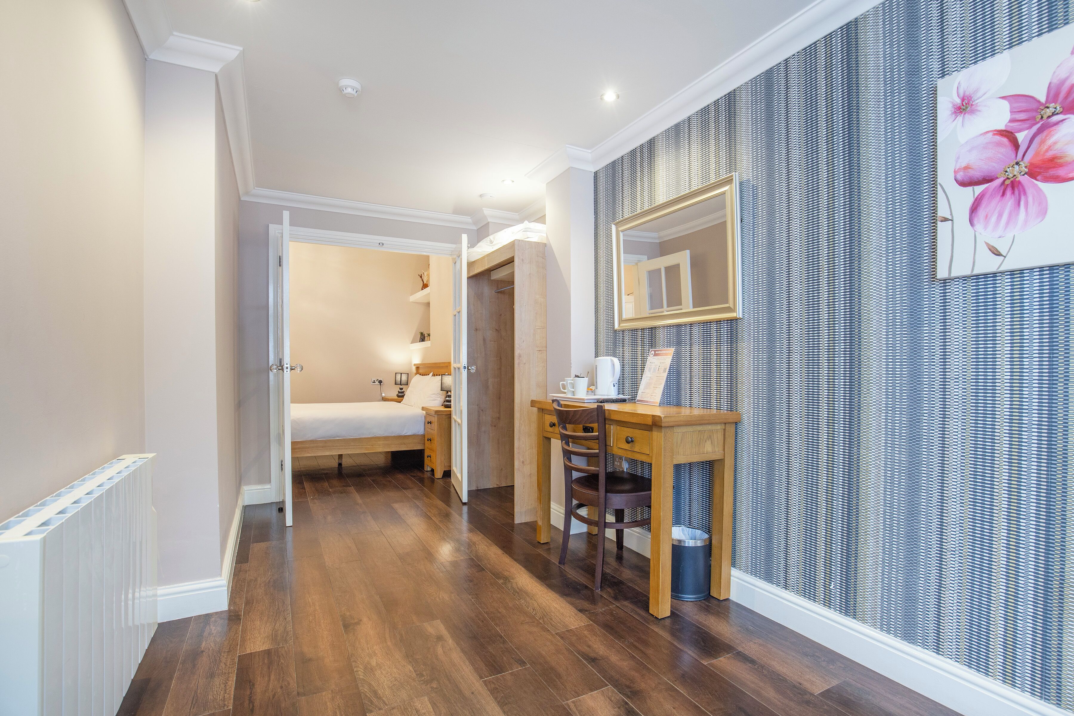 A hallway with a bed, a desk, and a trash bin.