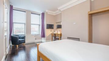 A bedroom with a large bed, a desk with a chair, a television, and a window with blinds.