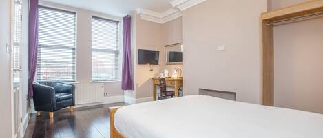 A bedroom with a large bed, a desk with a chair, a television, and a window with blinds.