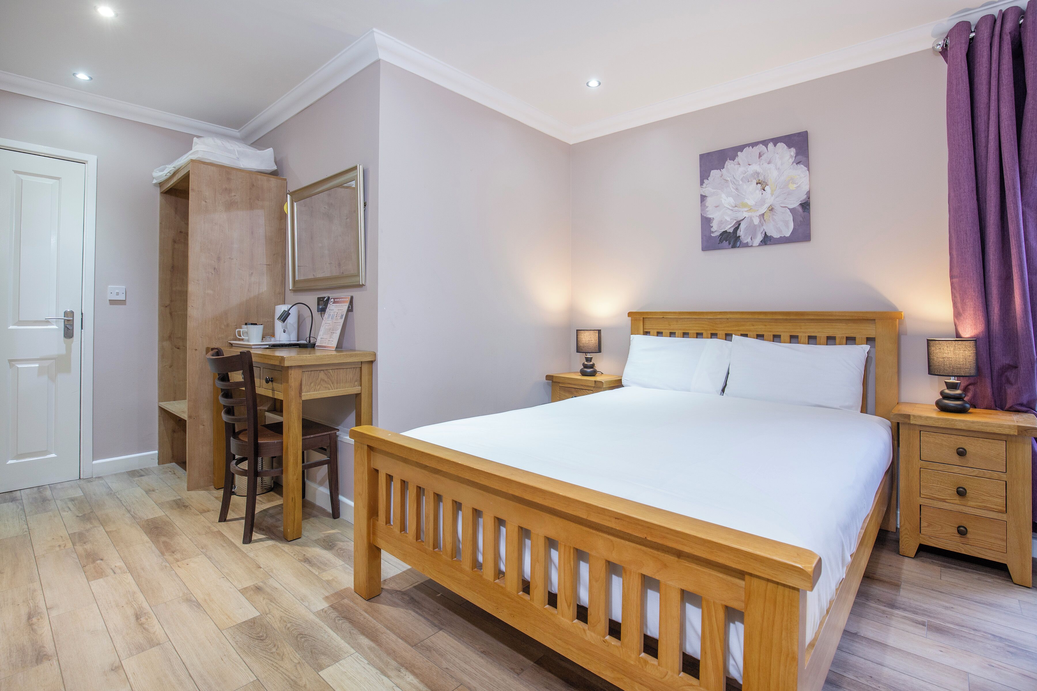 A bedroom with a wooden bed, bedside tables, a desk with a chair, and a mirror.