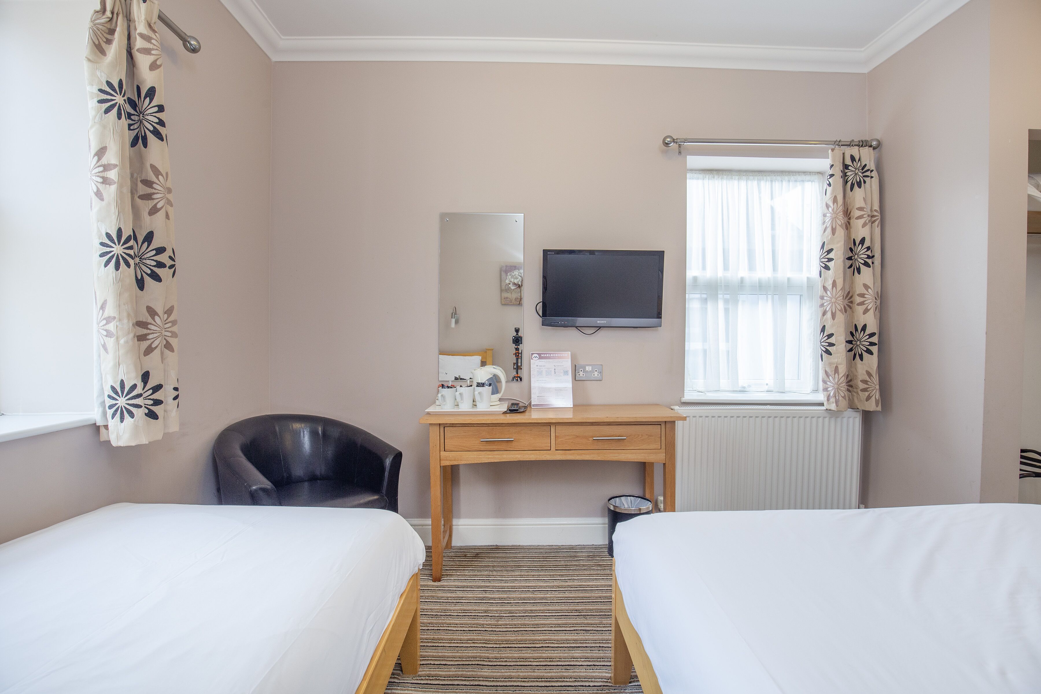 Une chambre d’hôtel avec deux lits simples, un bureau en bois équipé d’un téléviseur à écran plat, une chaise et un radiateur.