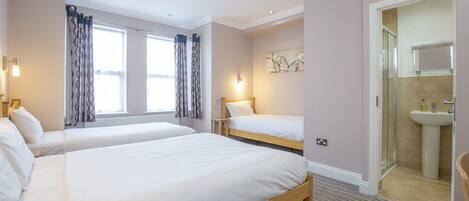 A hotel room with two beds, a bathroom with a sink, and a large window with curtains.