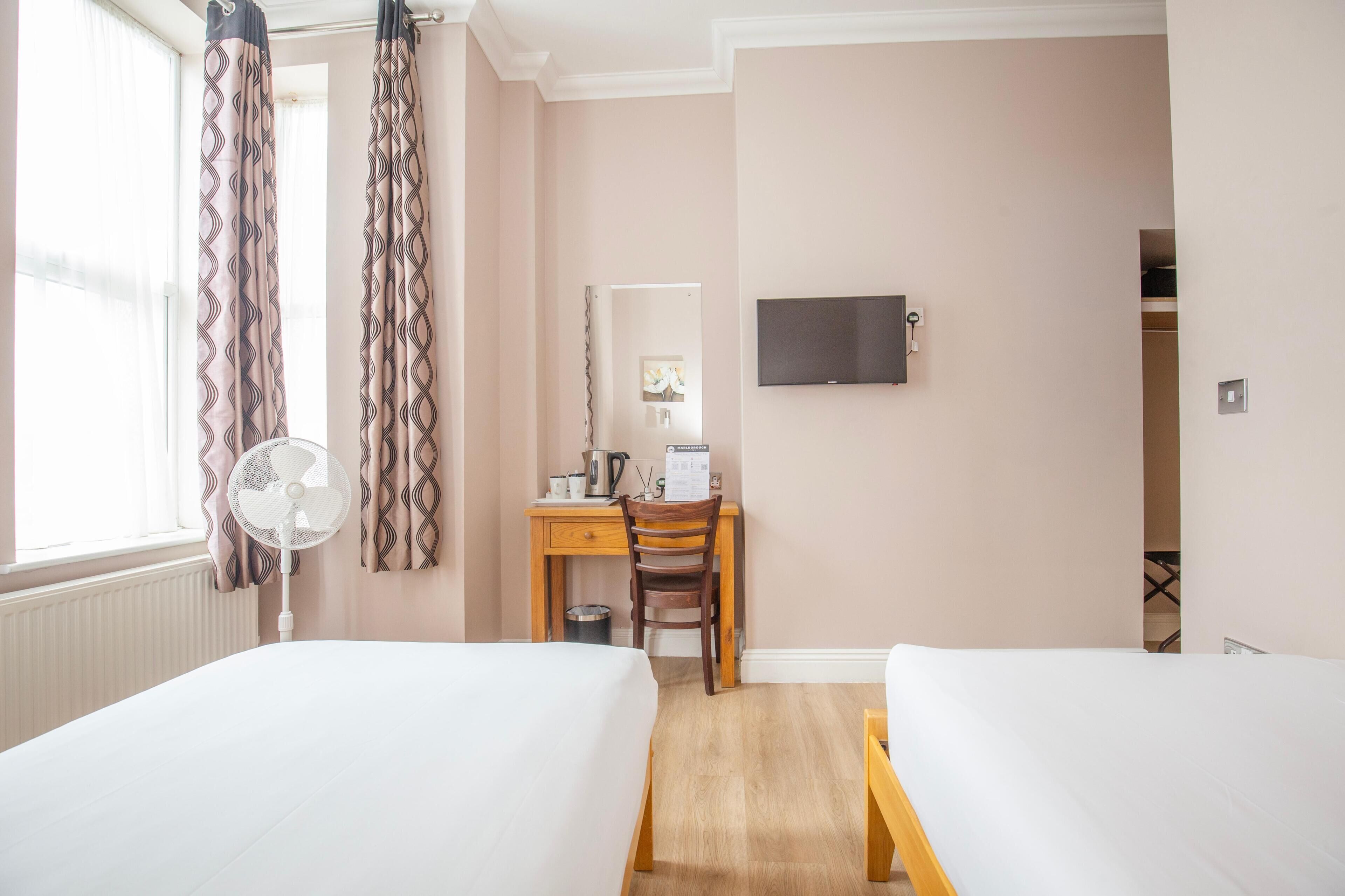 A hotel room with two beds, a desk with a chair, a TV mounted on the wall, and a window with curtains.