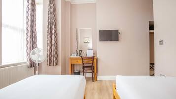A hotel room with two beds, a desk with a chair, a TV mounted on the wall, and a window with curtains.