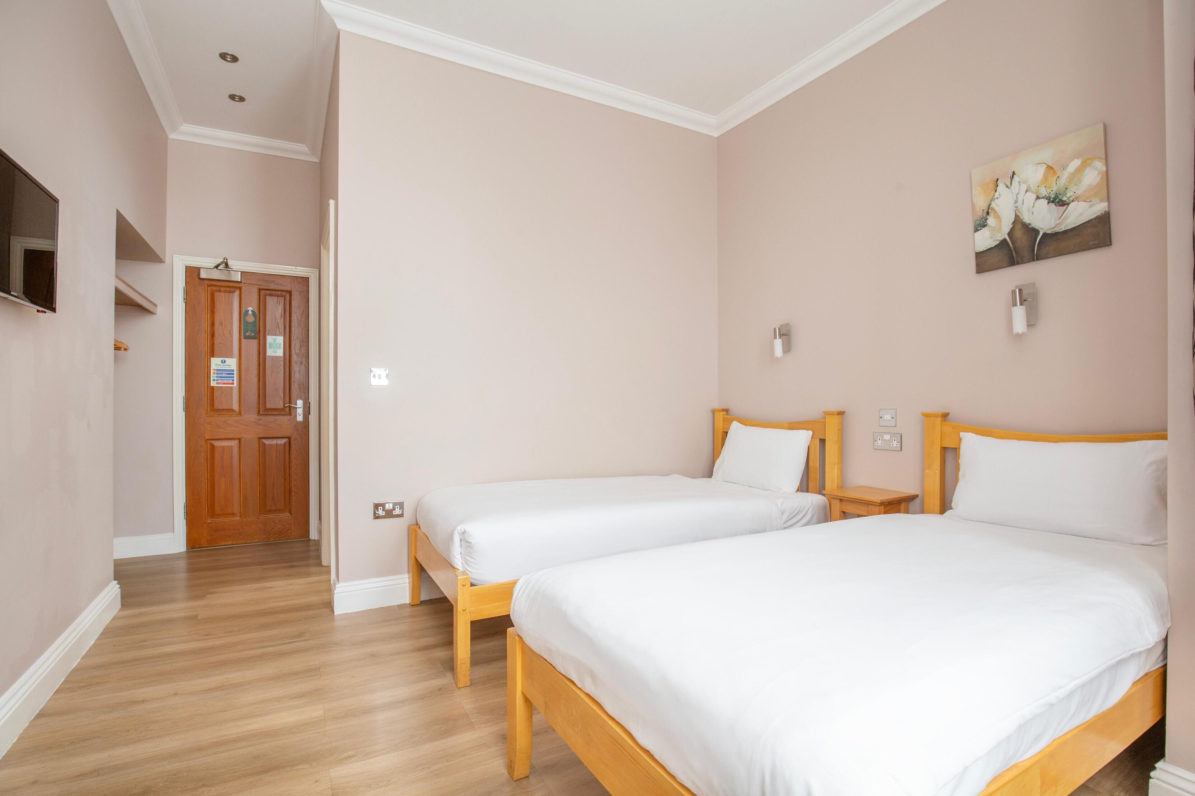 Ein Hotelzimmer mit zwei Betten, Holz-Kopfteilen, einem Bild an der Wand und einer Holztür mit einem Schild.