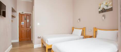 Een hotelkamer met twee bedden, houten hoofdborden, een schilderij aan de muur en een houten deur met een bordje.