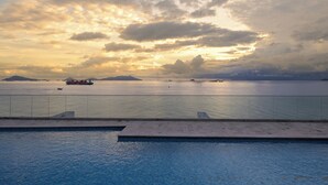 A swimming pool with a view of the sea and distant islands during sunset.