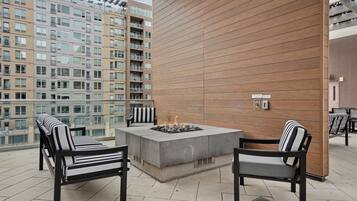 Una terraza en la azotea con un brasero, dos sillones de descanso y vistas a edificios altos.