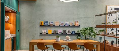 Ein moderner Essbereich mit einem Holztisch, vier Stühlen, einem Bücherregal mit Reiseführern und einer hängenden Leuchte.