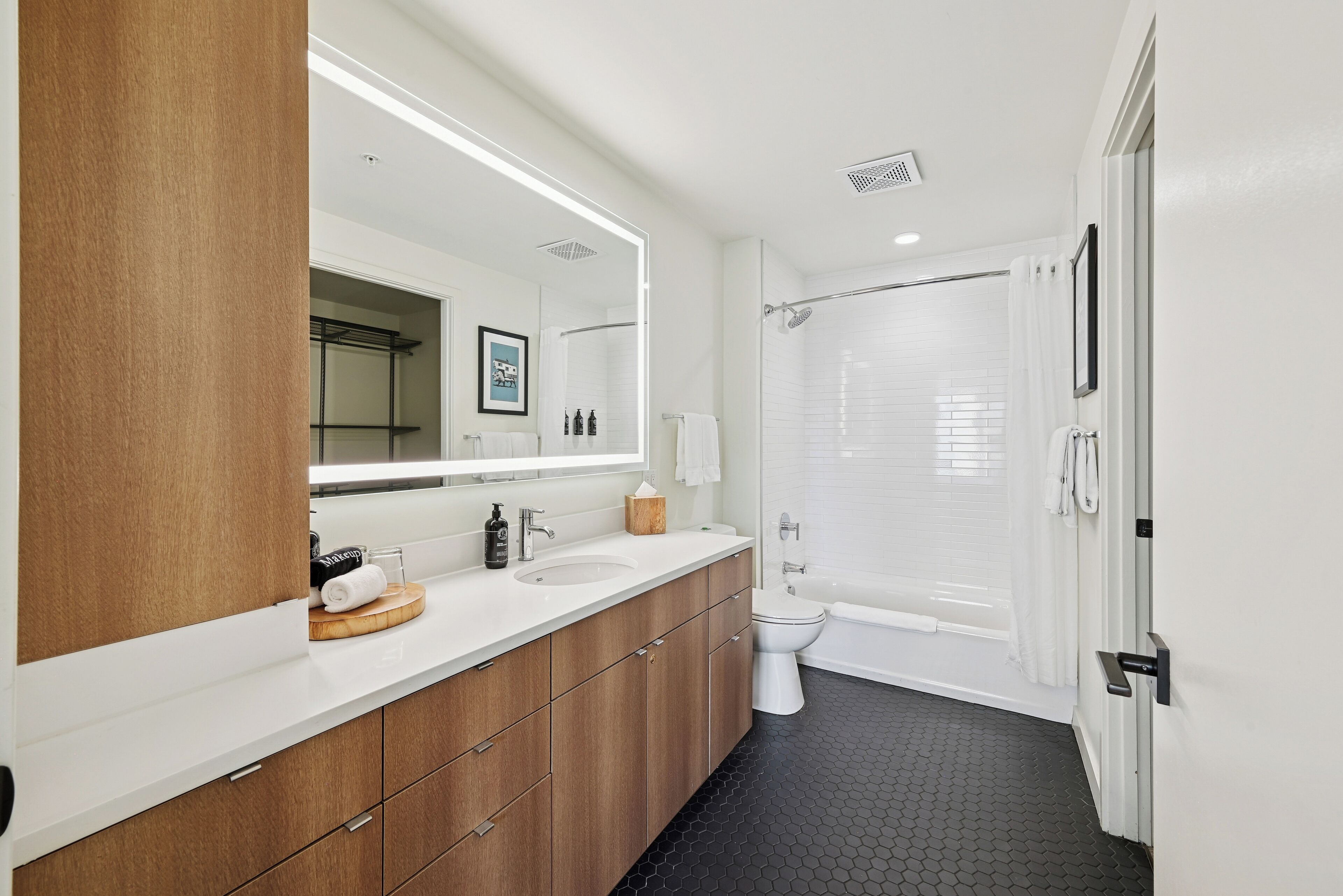 A modern bathroom with a white sink, wooden vanity, a large mirror, a toilet, and a bathtub.