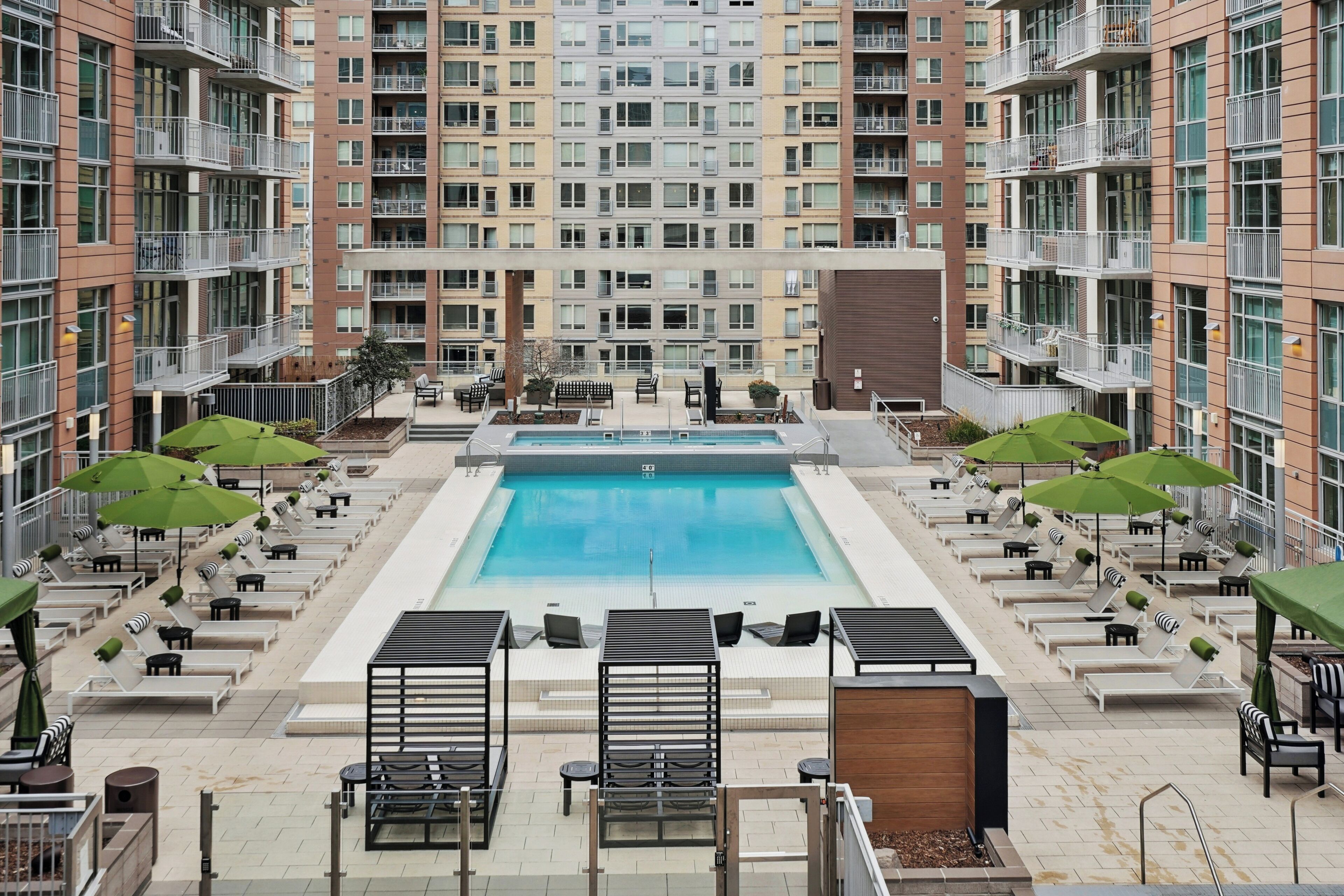 A rooftop pool area with lounge chairs and umbrellas, surrounded by high-rise residential buildings.