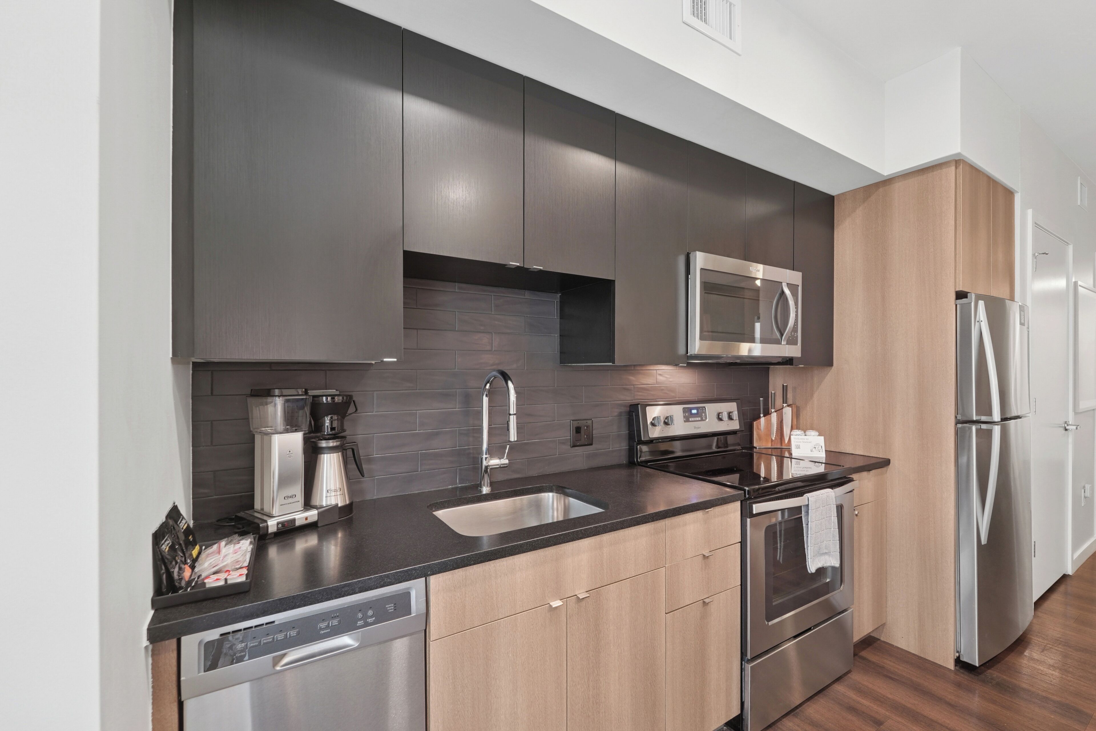 Una cucina moderna con mobili scuri, un frigorifero in acciaio inox, un forno a microonde, una macchina da caffè e una lavastoviglie.