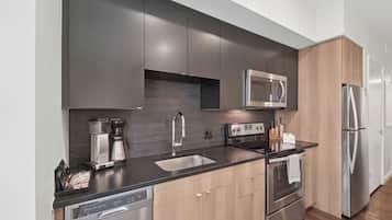 Una cucina moderna con mobili scuri, un frigorifero in acciaio inox, un forno a microonde, una macchina da caffè e una lavastoviglie.