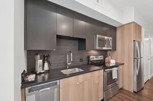 Una cucina moderna con mobili scuri, un frigorifero in acciaio inox, un forno a microonde, una macchina da caffè e una lavastoviglie.