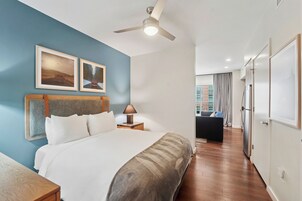 Habitación de hotel con cama, ventilador de techo, mesita de noche, lámpara y vistas de la ciudad a través de la ventana.