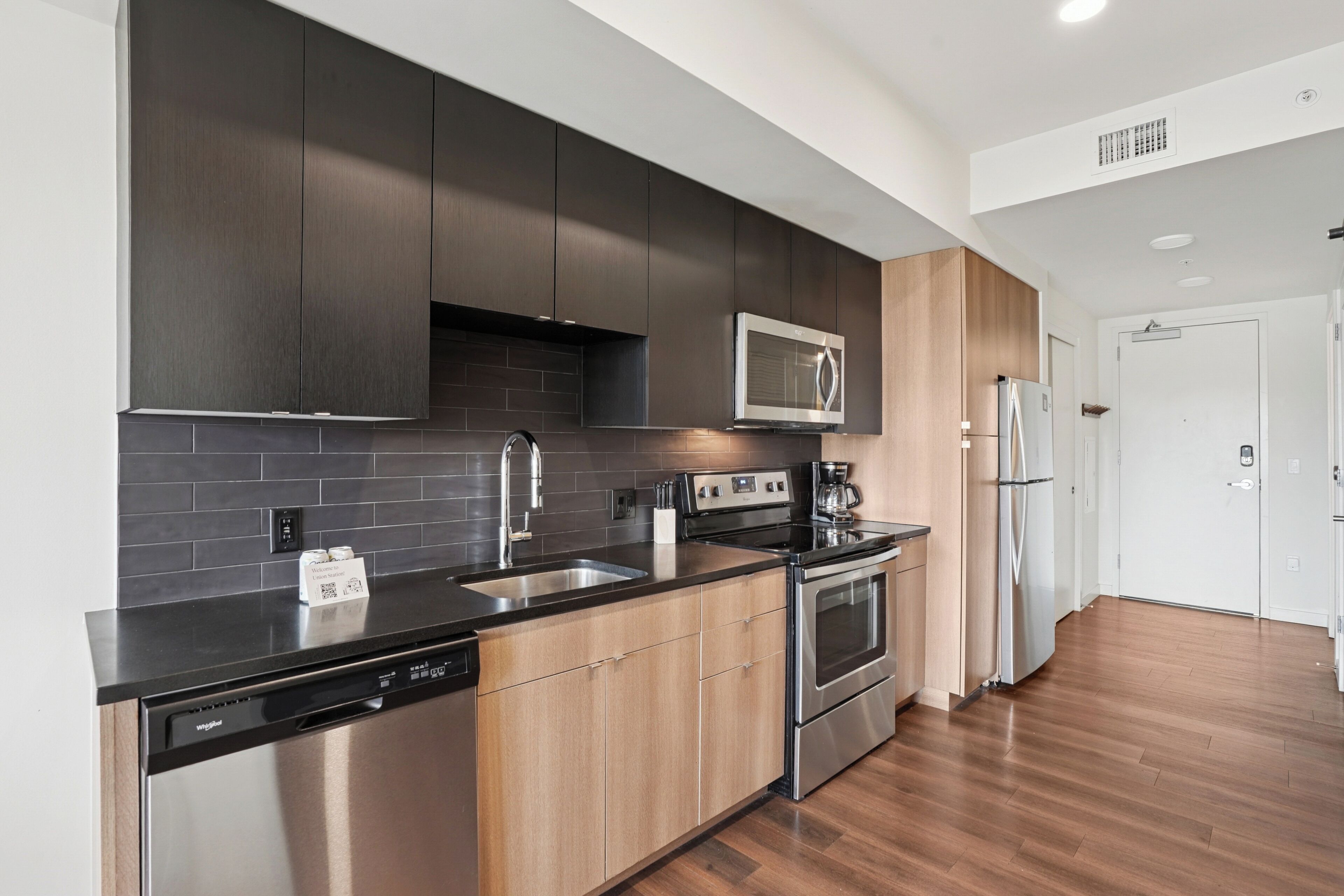 A modern kitchen with dark cabinetry, stainless steel appliances, and a black countertop.