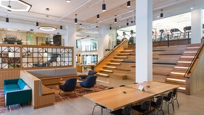 A modern interior with a wooden staircase, a seating area with a sofa and chairs, and a long table with chairs. - Sentral Union Station (Denver)