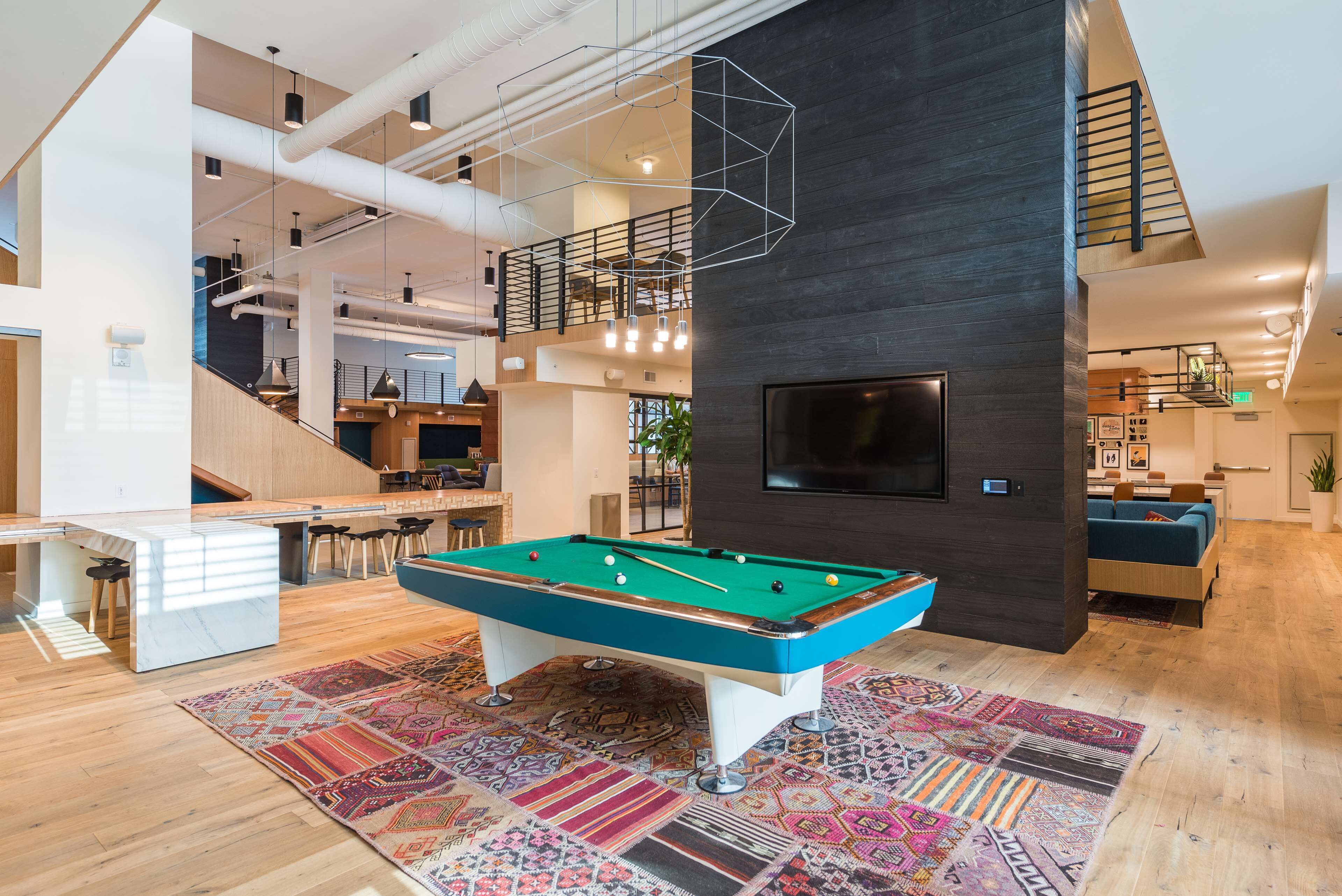 A modern living room with a pool table, a staircase, and a TV mounted on the wall.