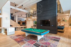 A modern living room with a pool table, a staircase, and a TV mounted on the wall.