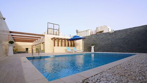 Una piscina con lettini prendisole e un pergolato, circondata da un cordolo di ciottoli e un muro in pietra.