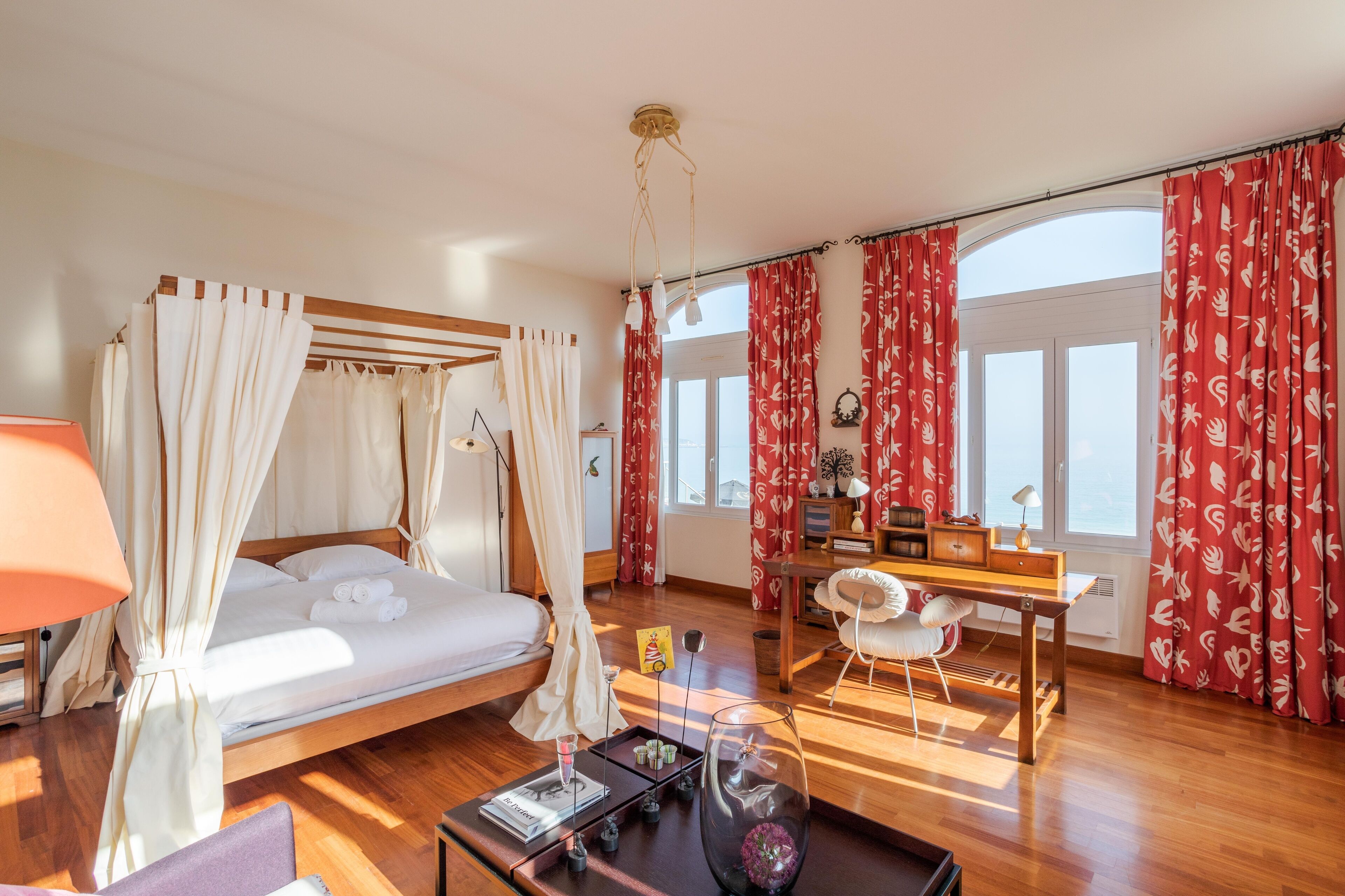 A bedroom with a canopy bed, a desk, and a view of the outdoors.