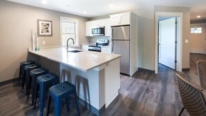 A modern kitchen with a large island, white cabinetry, stainless steel appliances, and a bar stool seating area. - Long Beach Suites: 3 Mins Toes To Sand! (Gloucester)