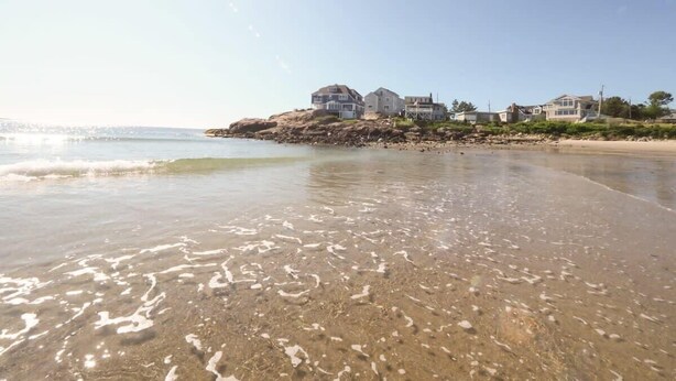 A beach with clear water and a rocky shoreline. There are houses on a cliff overlooking the beach. - Long Beach Suites: 3 Mins Toes To Sand! (Gloucester)