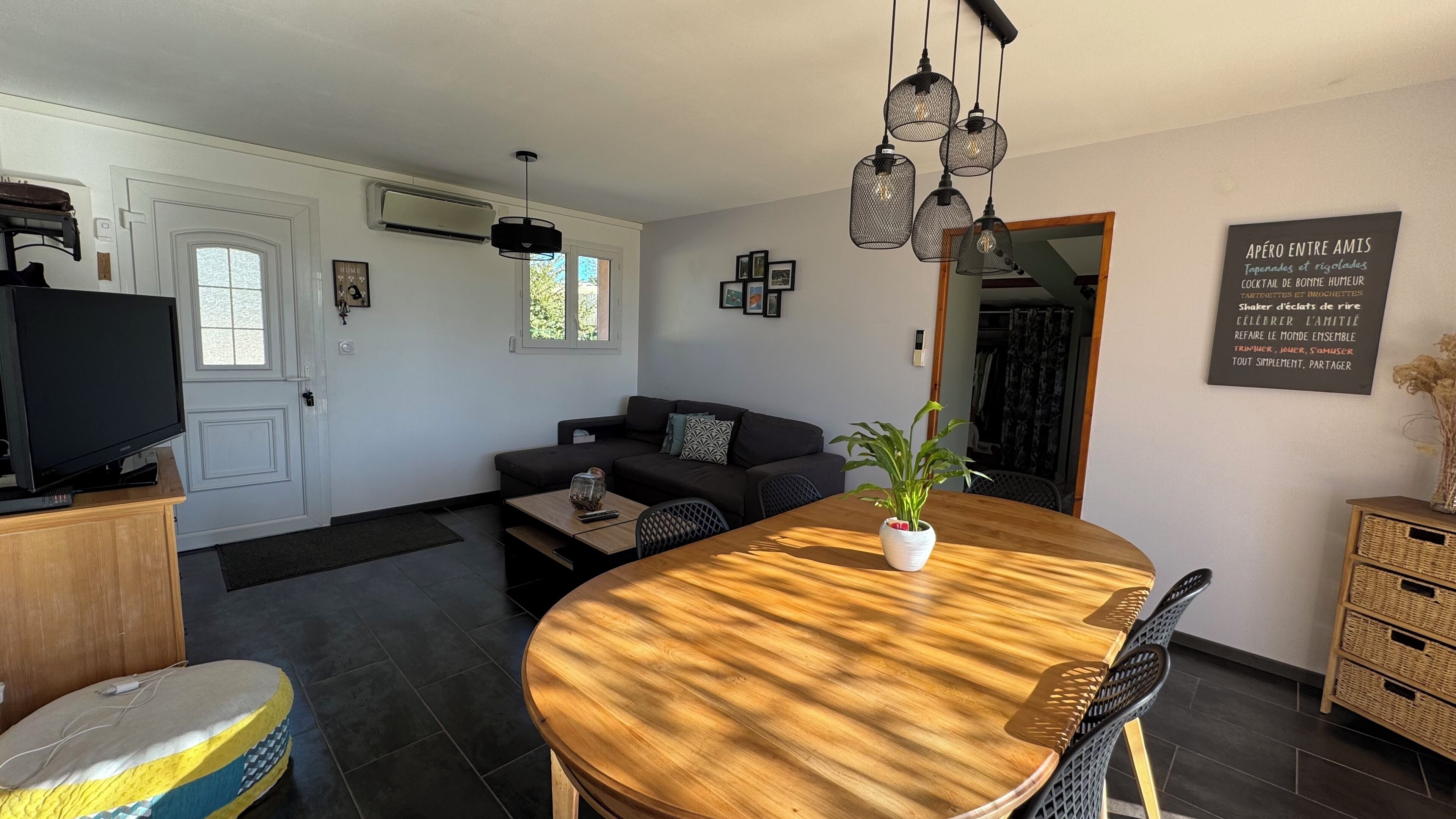 A modern living room with a wooden dining table, a sofa, a TV, and a wall-mounted air conditioner.