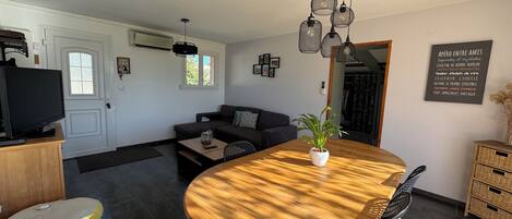 A modern living room with a wooden dining table, a sofa, a TV, and a wall-mounted air conditioner.